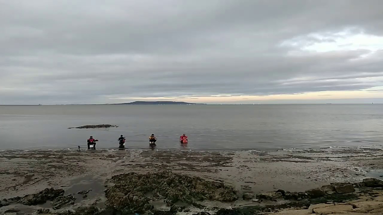 Tide Quartet - a shot of a beach with the tide out and a cello and four chairs on the sand